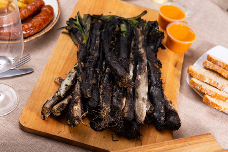 Traditional dishes of Catalonia, calcot with romesco sauce served on wooden board, bread and butifarra sausage on tableの写真素材