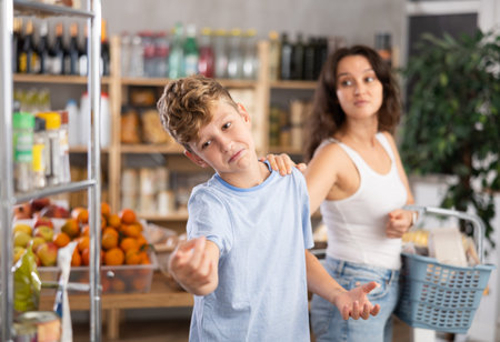 Capricious teenage boy wants to buy lot of sweets, but his mother does not allow him. Family quarrel in supermarketの写真素材