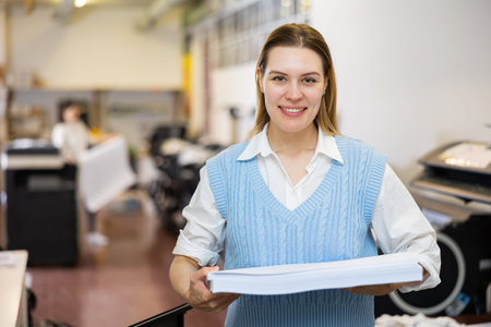 Cheerful woman printing shop manager holding ream of paper