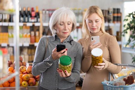 Elderly mother and her adult daughter scan QR code on jar canned green olives label together to check expiration dateの写真素材