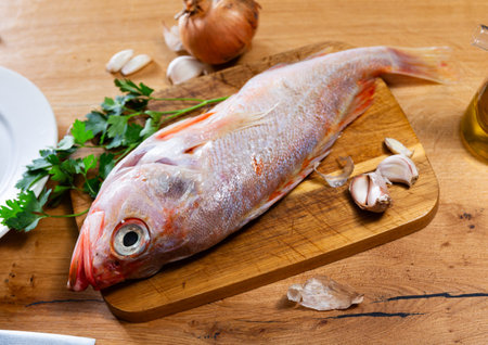 Raw whole red palometa fish with garlic and parsley on desk