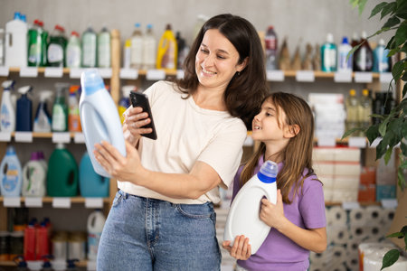 Mother and daughter checking expiration date of detergent using her smartphone in supermarketの写真素材