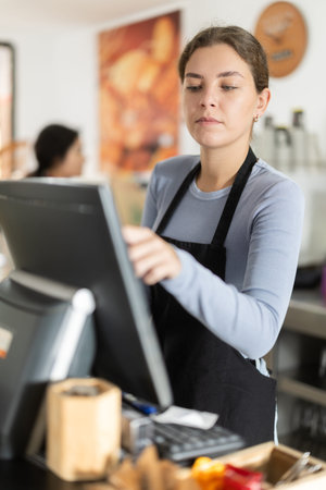 Attentive young waitress checking orders on monitor in cafeteria