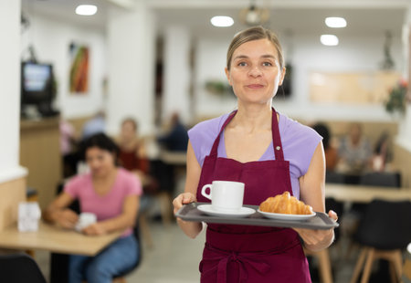 Polite waitress holding tray with coffee and croissant in cafeteriaの写真素材