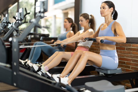 Sportive young girls training on cable row machine in gym