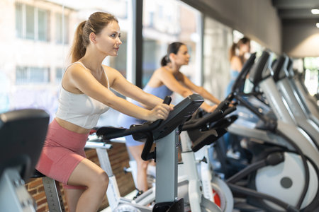 Smiling young girl doing spin bike exercises in well-equipped gymの写真素材