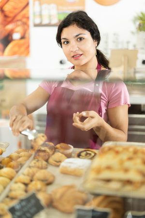 Woman seller putting fresh pastries on plate in cafe bakeryの写真素材