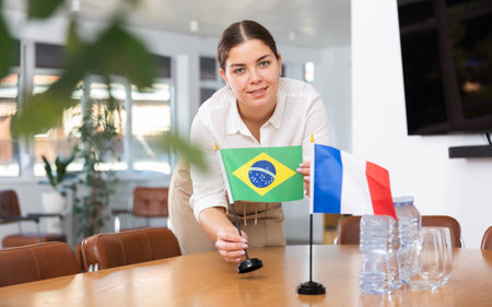 Positive young woman putting flag of Brazil on the table with flag of France in conference roomの写真素材