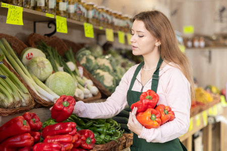 Young woman seller puts pepper in vegetable shopの写真素材