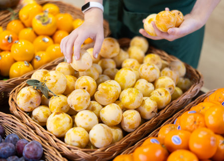 Female salesperson places yellow plums on display case. Closeup of salesperson hands and yellow...
