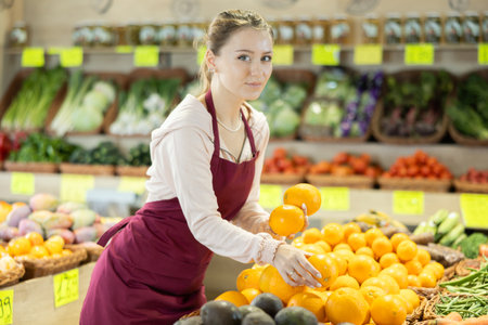 Young woman seller puts oranges in vegetable shopの写真素材