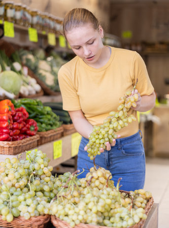 Teenage girl chooses grapes in storeの写真素材
