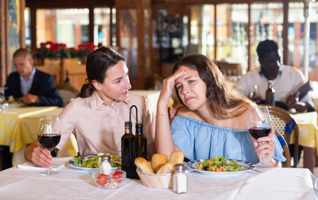 Girl complains to her friend at a table in restaurantの写真素材