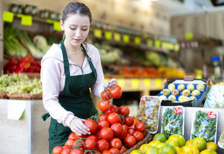 Young woman seller puts tomatoes in vegetable shopの写真素材