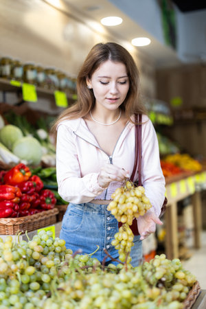 Girl selects ripe grapes from counter in grocery storeの写真素材