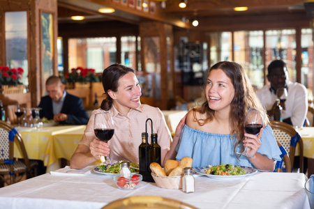 Two positive female best friends drinking wine in restaurantの写真素材
