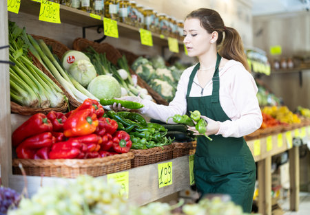 Woman employees in uniform holding fresh bell pepper in grocery shopの写真素材