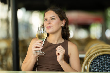 Beautiful woman relaxing and drinking white wine while sitting on terrace of street cafe of Barcelonaの写真素材
