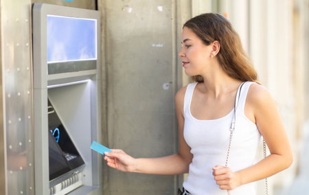 Young girl withdrawing cash from ATM on city streetの写真素材