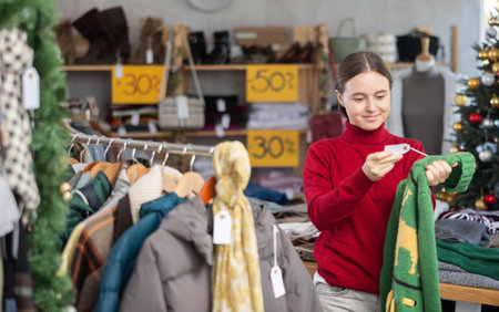 Teen girl picks up clothes and chooses sweater, New Year Eve saleの写真素材