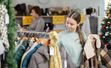 In sales area of store during Christmas sale, teen girl customer choose down jacket