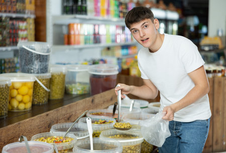Guy in supermarket scooping marinated green olives into plastic bagの写真素材