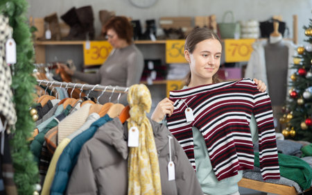 Teen girl picks up clothes and chooses sweater, New Year Eve saleの写真素材