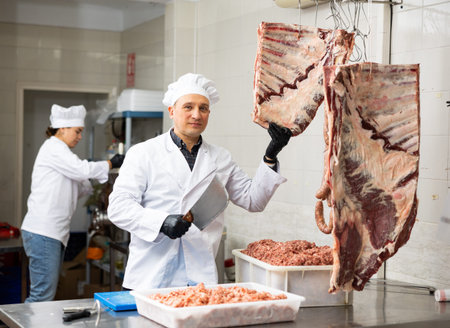 Positive male butcher preparing big piece of beef meat in butcher shopの写真素材