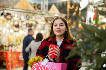 Girl with paper cup of tea walking at street Christmas fairの写真素材