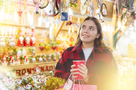 Girl holding paper cup while enjoying a walk through the traditional city street fair on Christmas Eveの写真素材