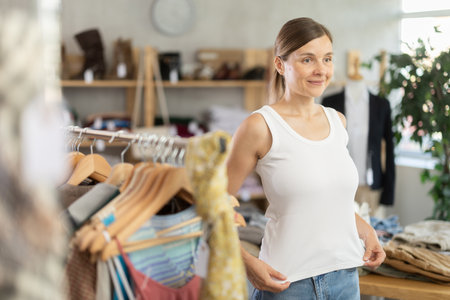 Adult woman trying on white tank top in storeの写真素材