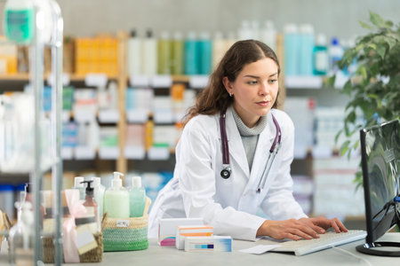 Portrait of young female pharmacist working at computer in pharmacyの写真素材