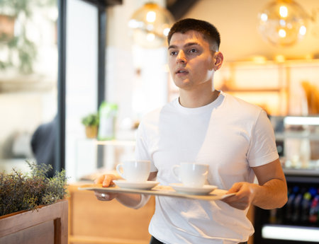 Young man with coffee walking to table in cafeの写真素材
