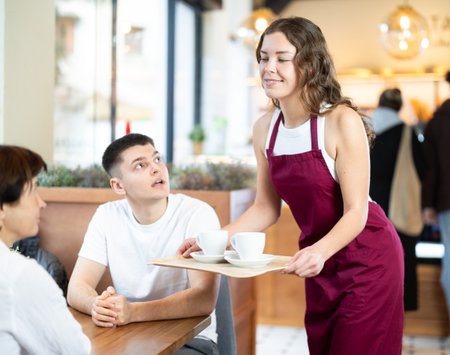 Young female waiter serving coffee to man and womanの写真素材