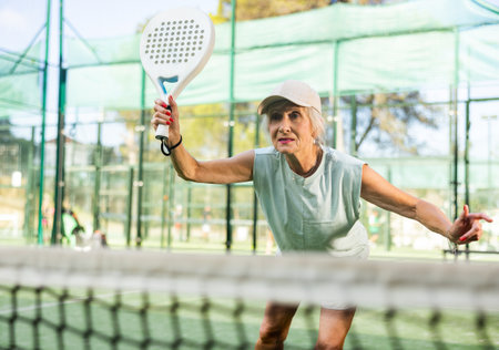 Concentrated elderly woman padel player hitting ball with a racket on hard courtの写真素材