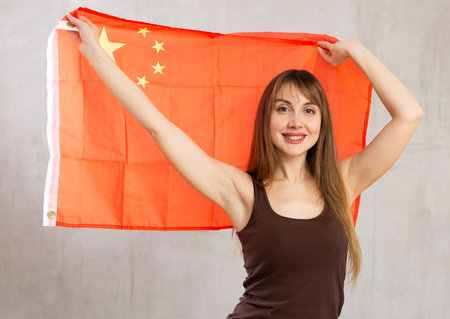 Happy young woman holding flag of China against unicoloured backgroundの写真素材