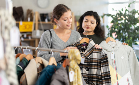 Two happy young women choosing coat or jacket for cold season in clothing shop with large assortmentの写真素材