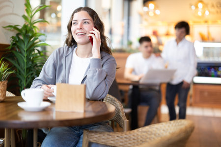 Girl in cafe drinks coffee and calling using mobile phoneの写真素材