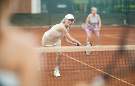 Two elderly women playing doubles tennisの写真素材