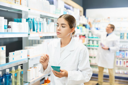 Girl pharmacist carefully reads the information on the label of a medicinal hygiene in pharmacyの写真素材