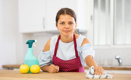 Positive woman cleaning kitchen table at home