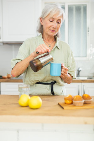 Old woman pouring coffee, having breakfast at homeの写真素材