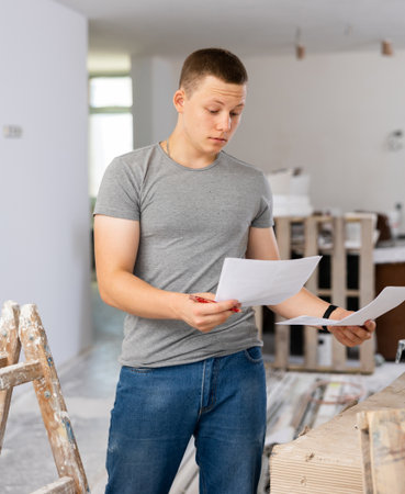 Young man checking project documentation in apartment during repair worksの写真素材