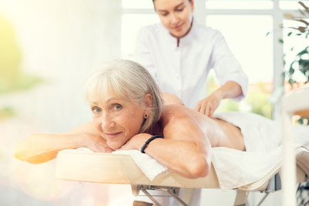 Smiling senior woman lying on couch during back massageの写真素材