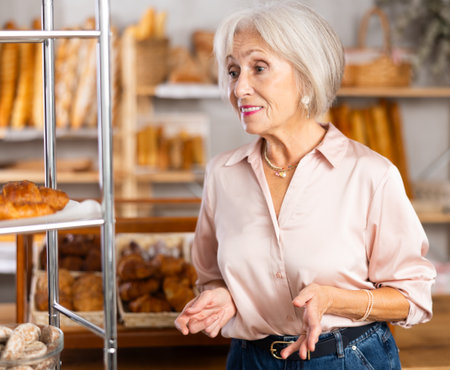 Mature female customer choosing bread and other delicious pastries in bakeryの写真素材