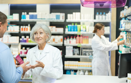 Male customer consulting with mature female pharmacist at pharmacyの写真素材