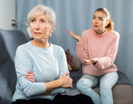 Agitated adult daughter reprimanding upset senior woman on sofaの写真素材