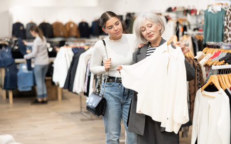 Two satisfied female customers choosing cardigan or jacket in clothing boutique
