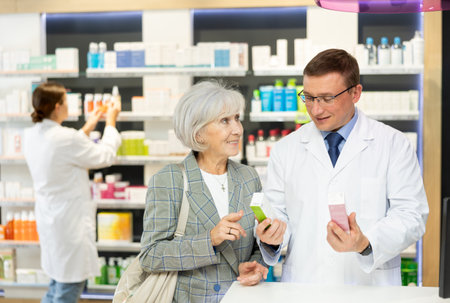 Man apothecary hold package with cream and talks with senior woman client about nuances of careの写真素材