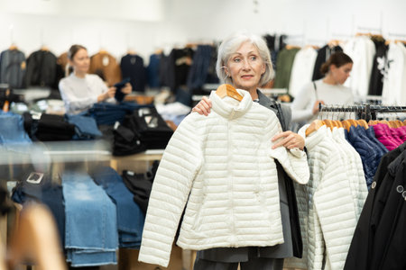 Old woman choosing white jacket in clothing storeの写真素材